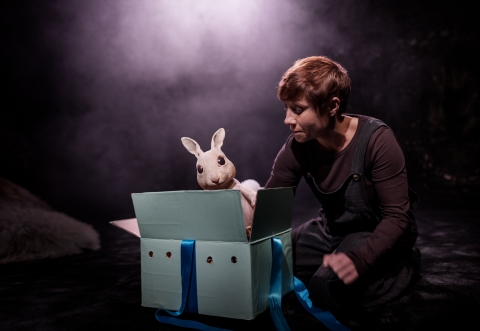 En kvinna tittar på en kanindocka som kommer upp ur en låda. 